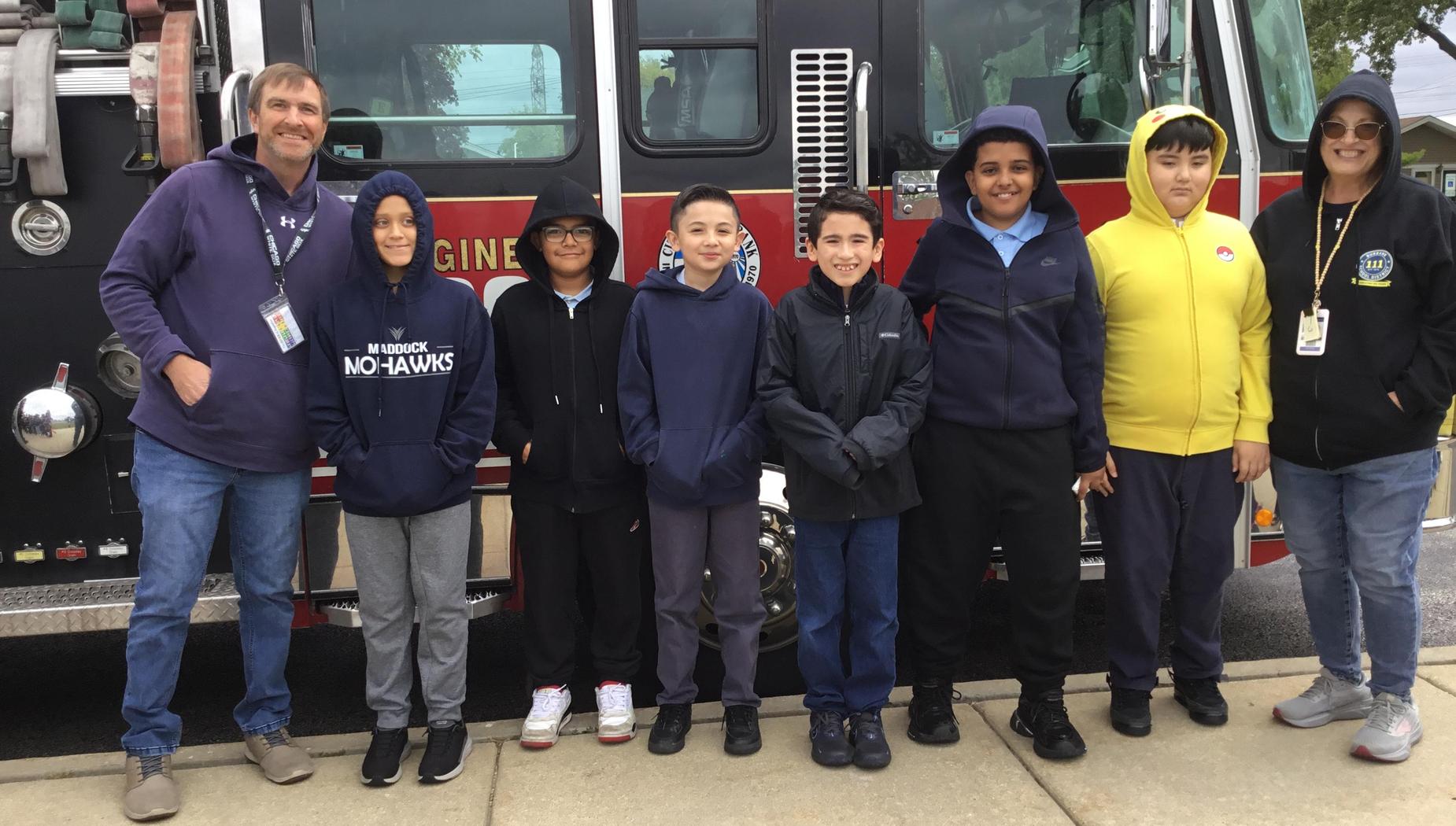 A group of seven people, including six children, stand in front of a fire truck.