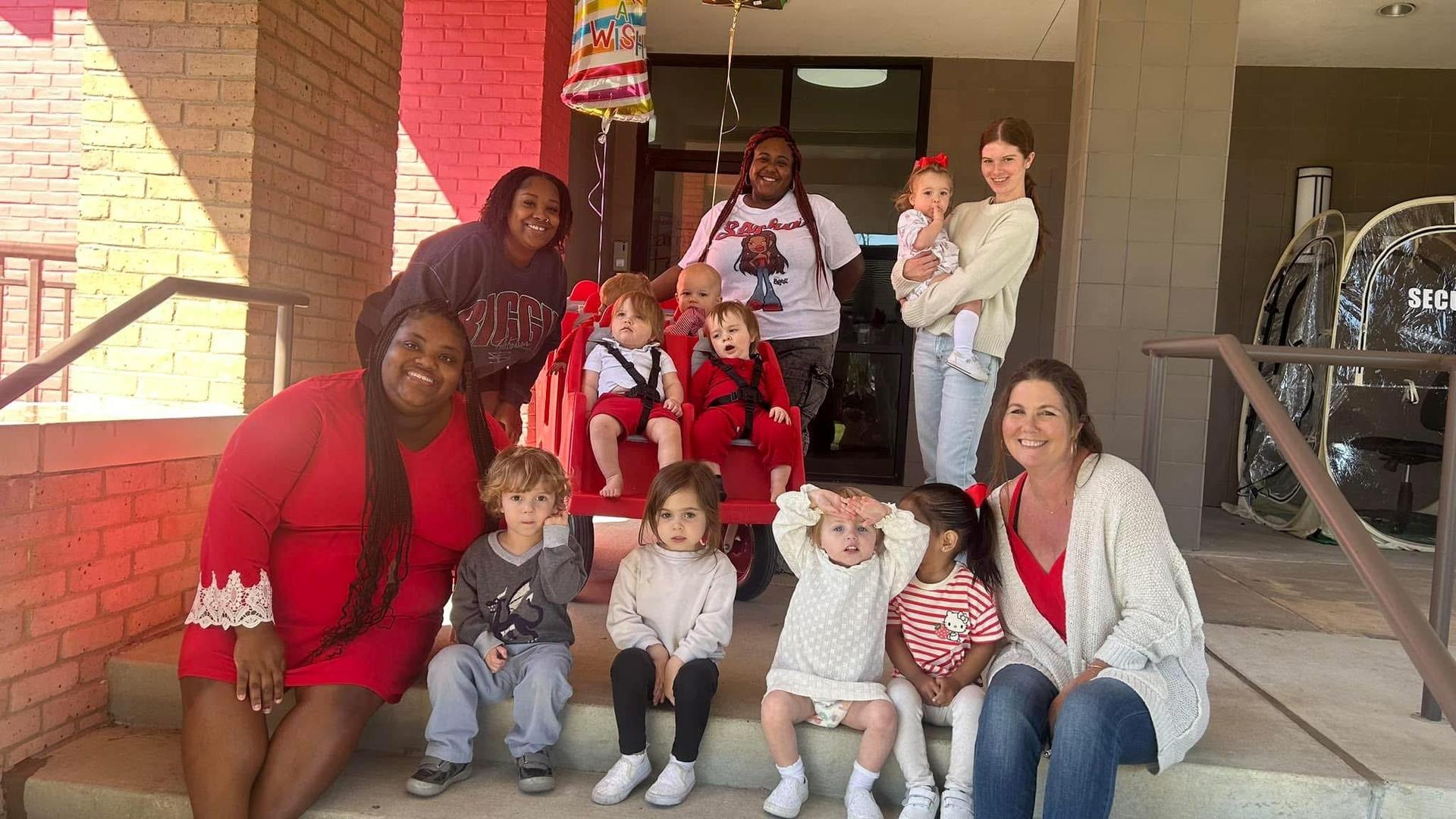 A group of adults and children posing together outside a building, celebrating with balloons.