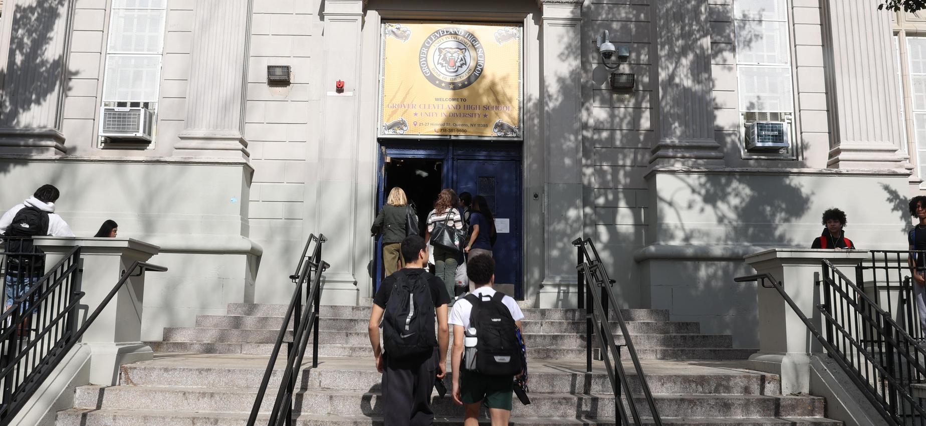 Students walking up steps to a school entrance with a banner above the door.