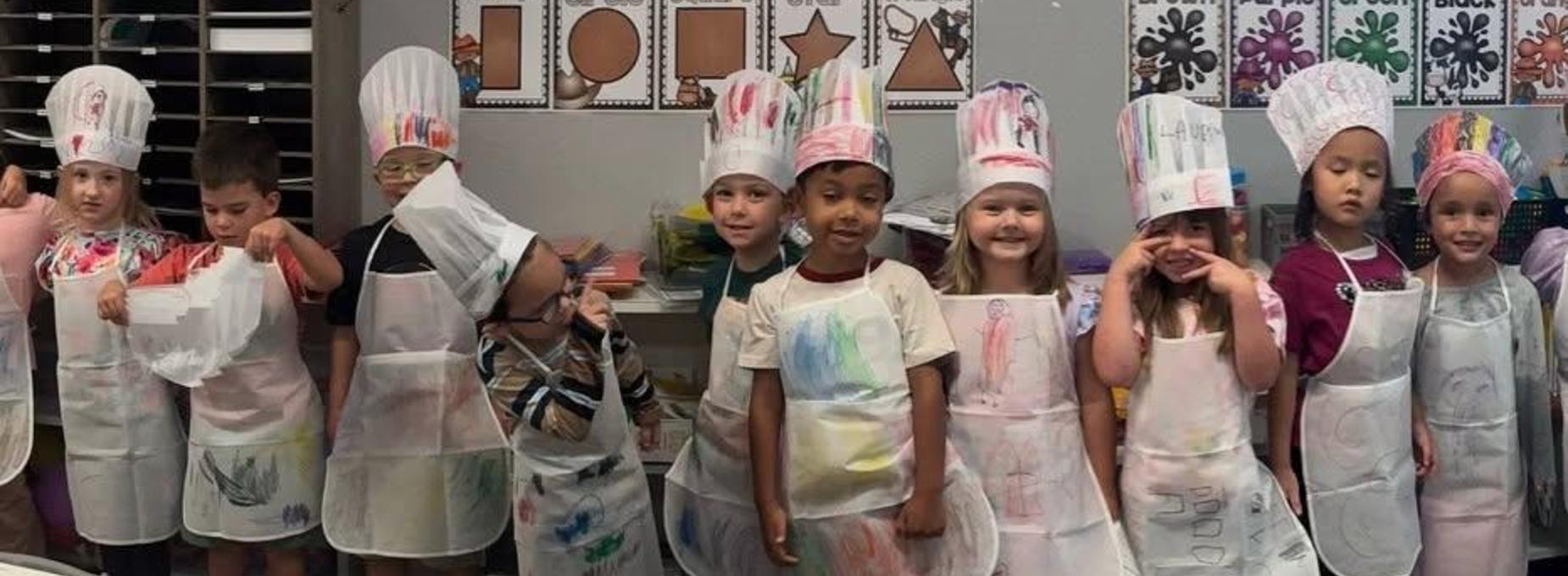 Children dressed as chefs wearing decorated hats and aprons.