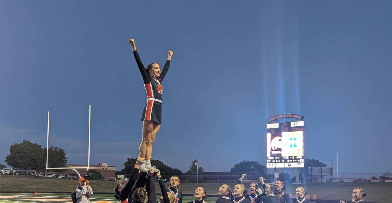 A TKHS cheerleader stands tall lifted in the air by her teammates.