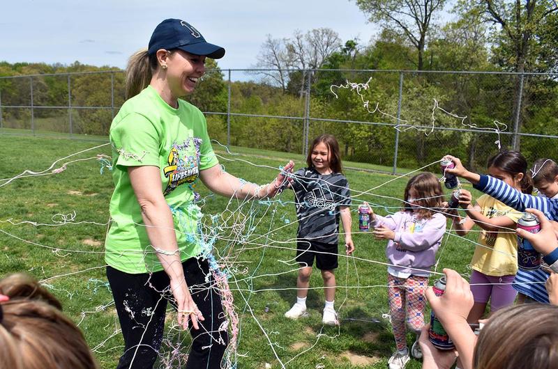 children spraying silly string at a woman wearing green