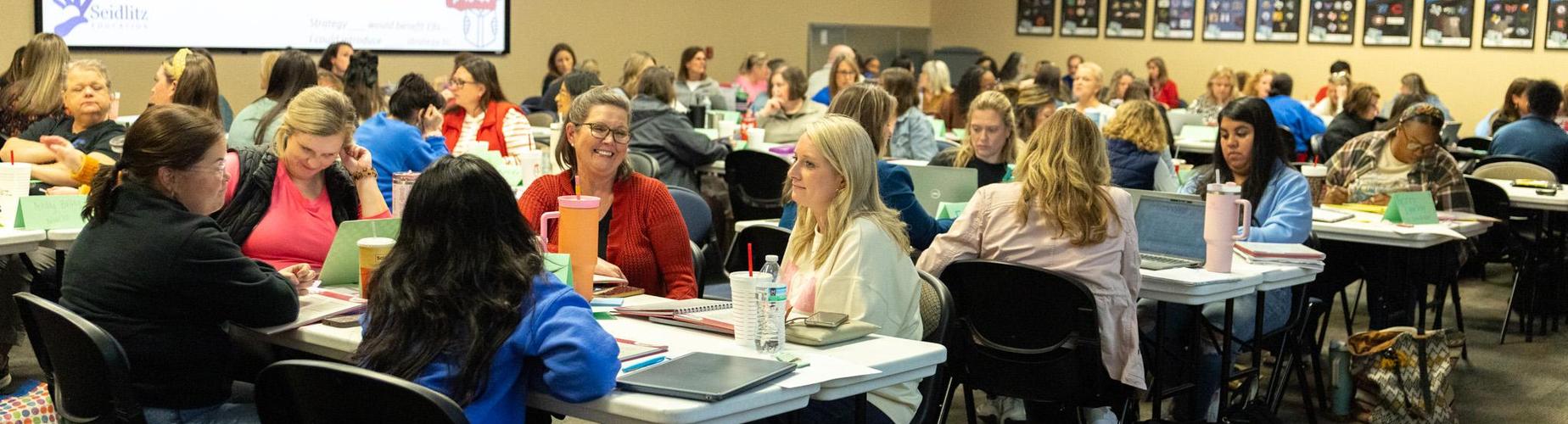 A large group of people engaging in a workshop or meeting at tables.
