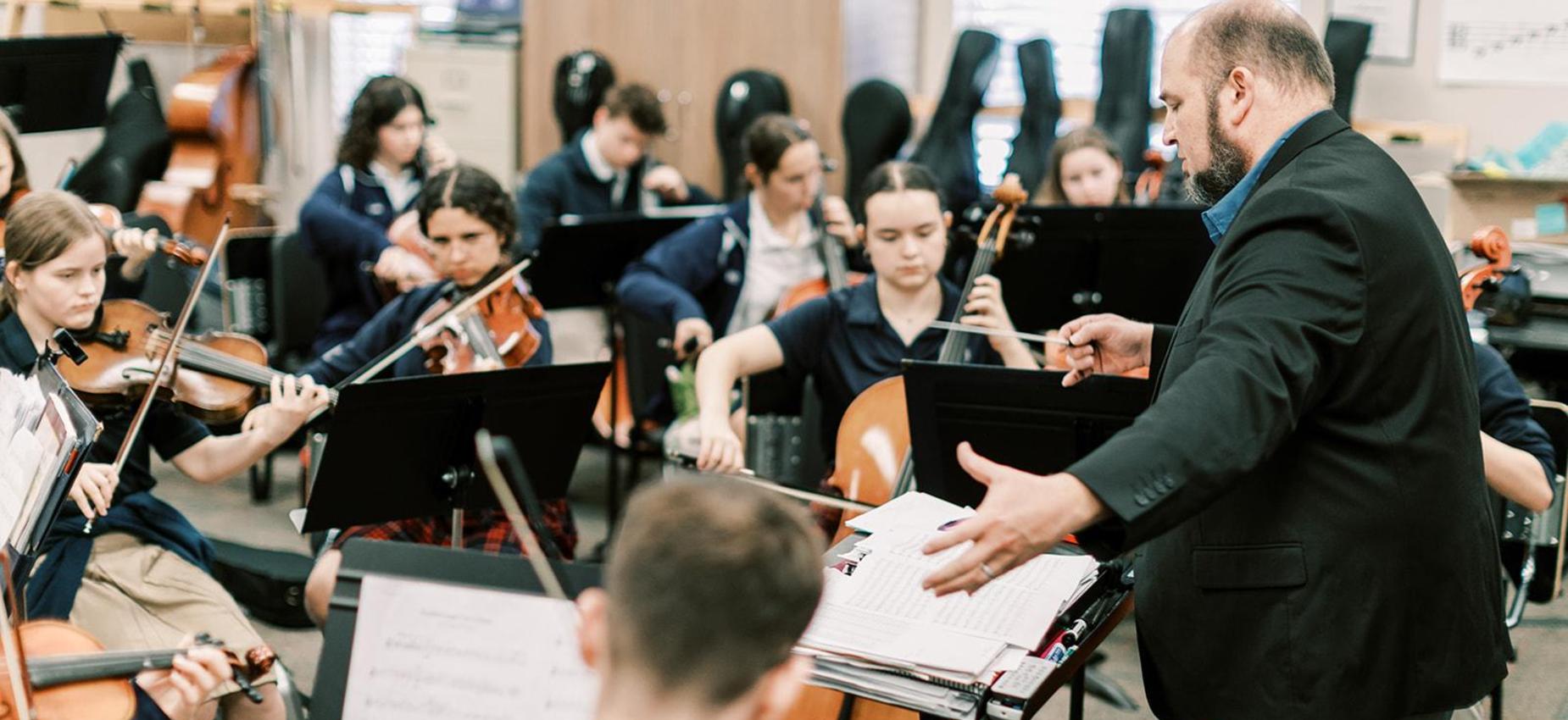 Orchestra teacher conducts student string musicians