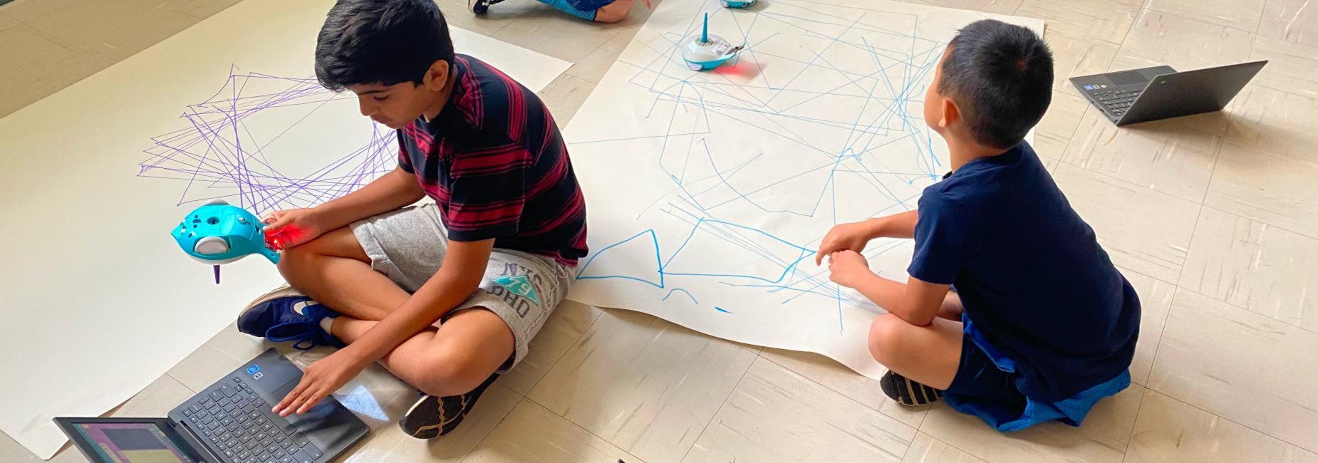 Elementary school students coding Finch robots to draw polygons.