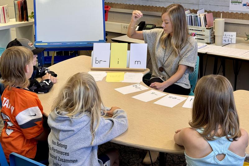 A teacher points to words on a card while students watch