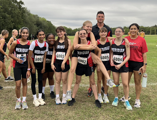 Girls' Cross Country participants stand in the field with coaches. Their uniforms are black and red. 