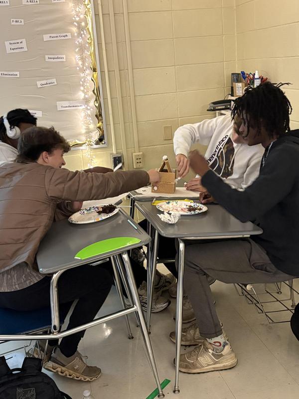 four students working on gingerbread house