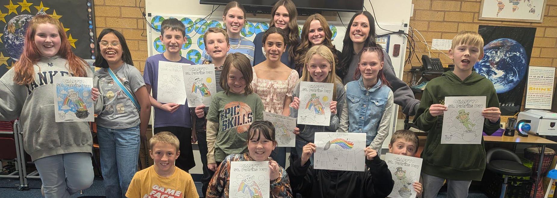 Students holding colorful artwork in a classroom setting.