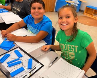 Two children smiling while working at their desks.