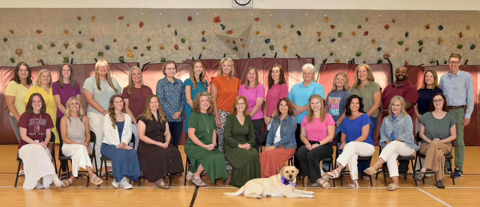 South staff pose in their gym smiling in two rows with their school dog laying down in front