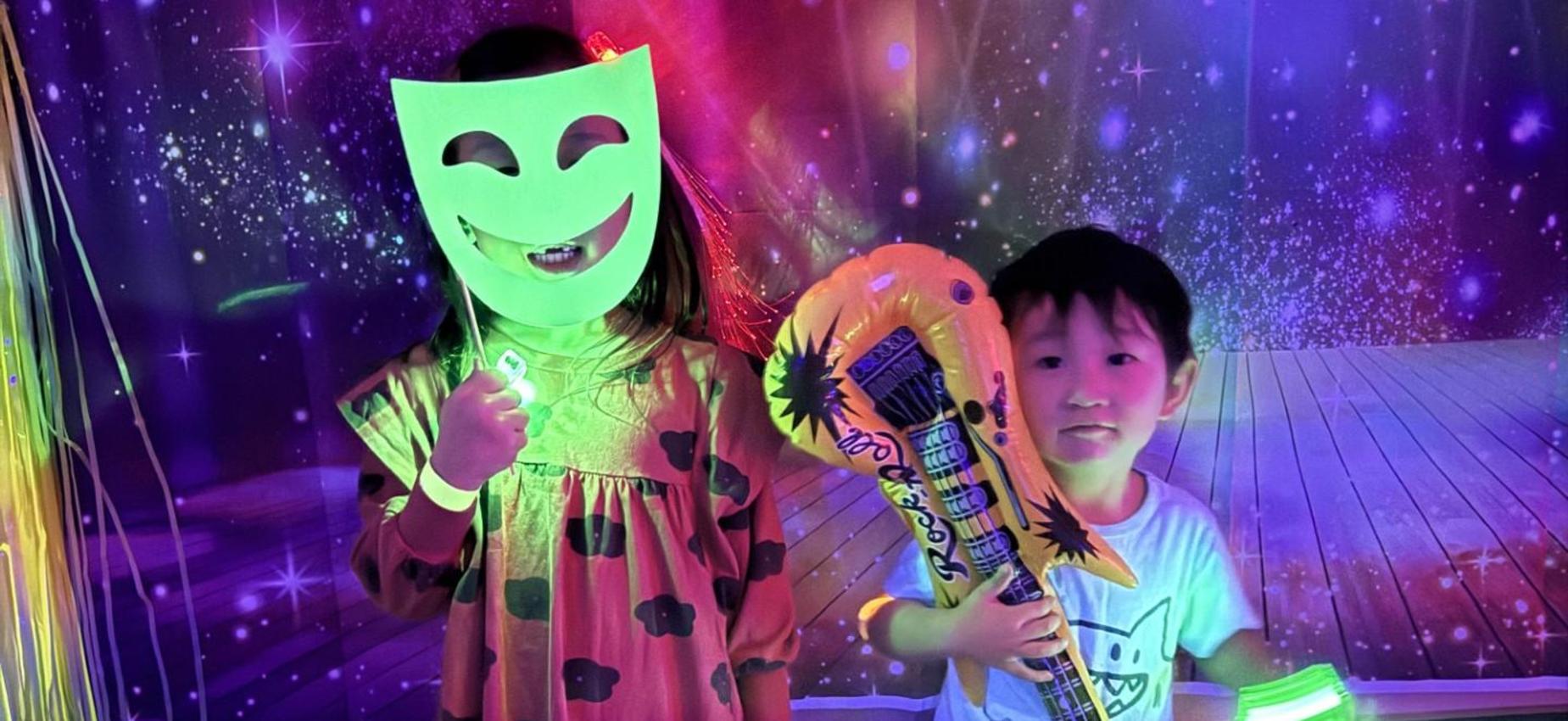 Two kids posing with playful props and glowing accessories at a themed event.
