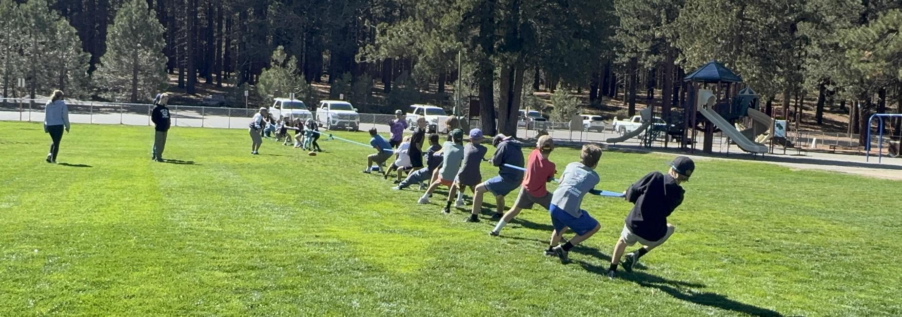A group of children participating in a tug-of-war on a grassy field.