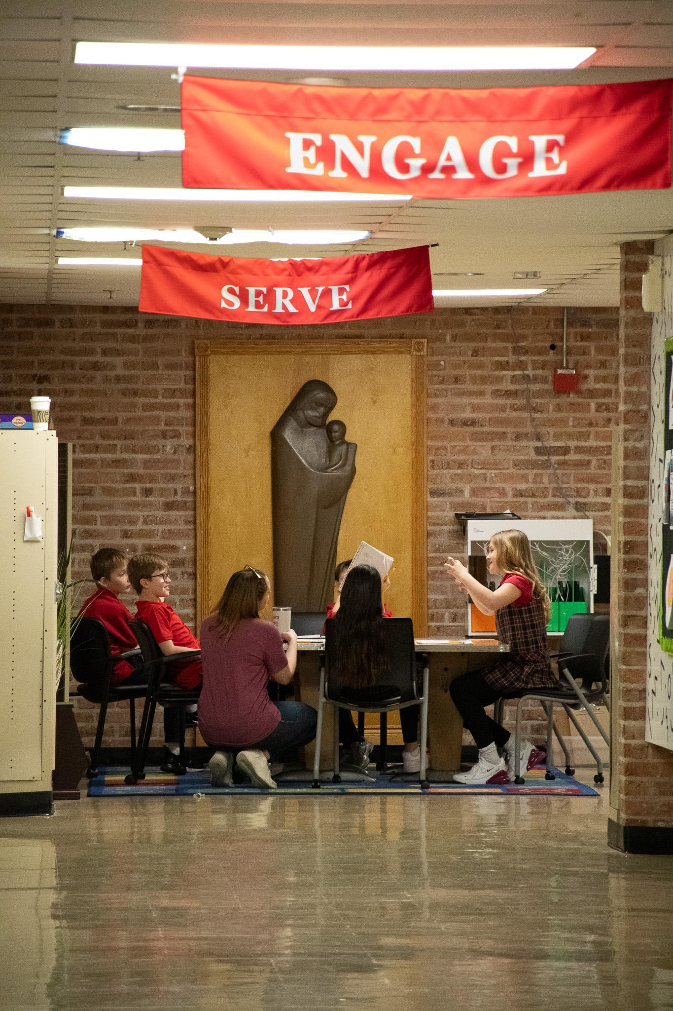 Students study at table with teacher under Engage sign