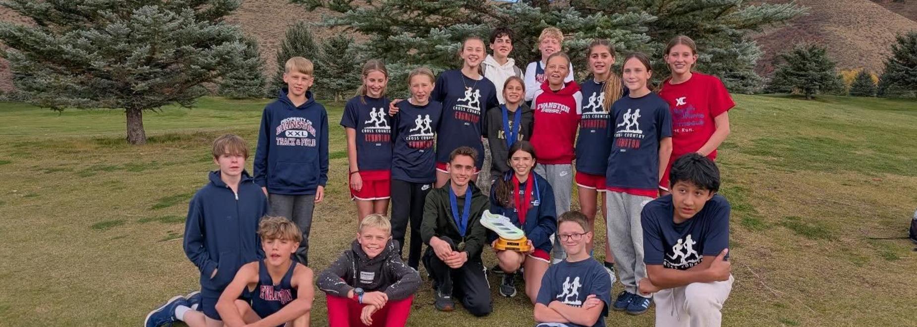 Group photo of a cross country team posing outdoors among trees and mountains.