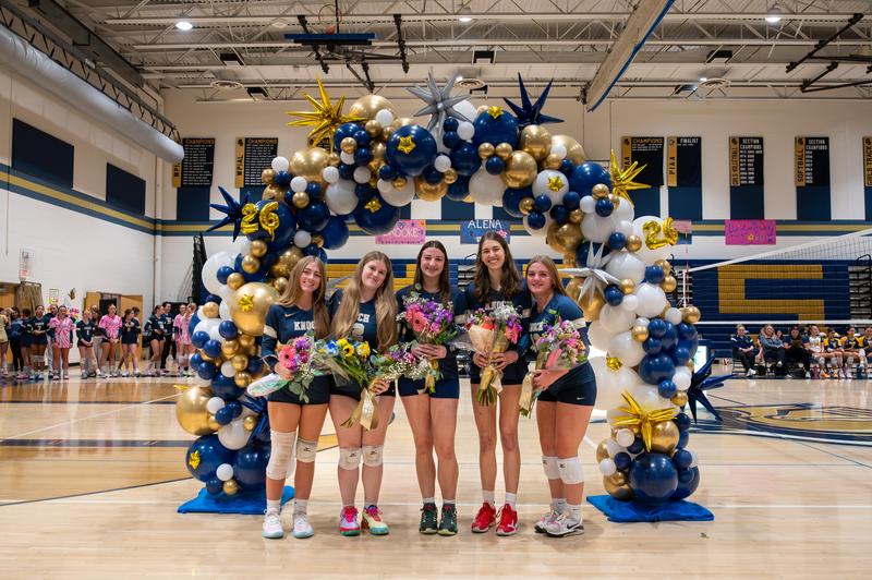 girls in uniforms standing in a gym with a balloon arch