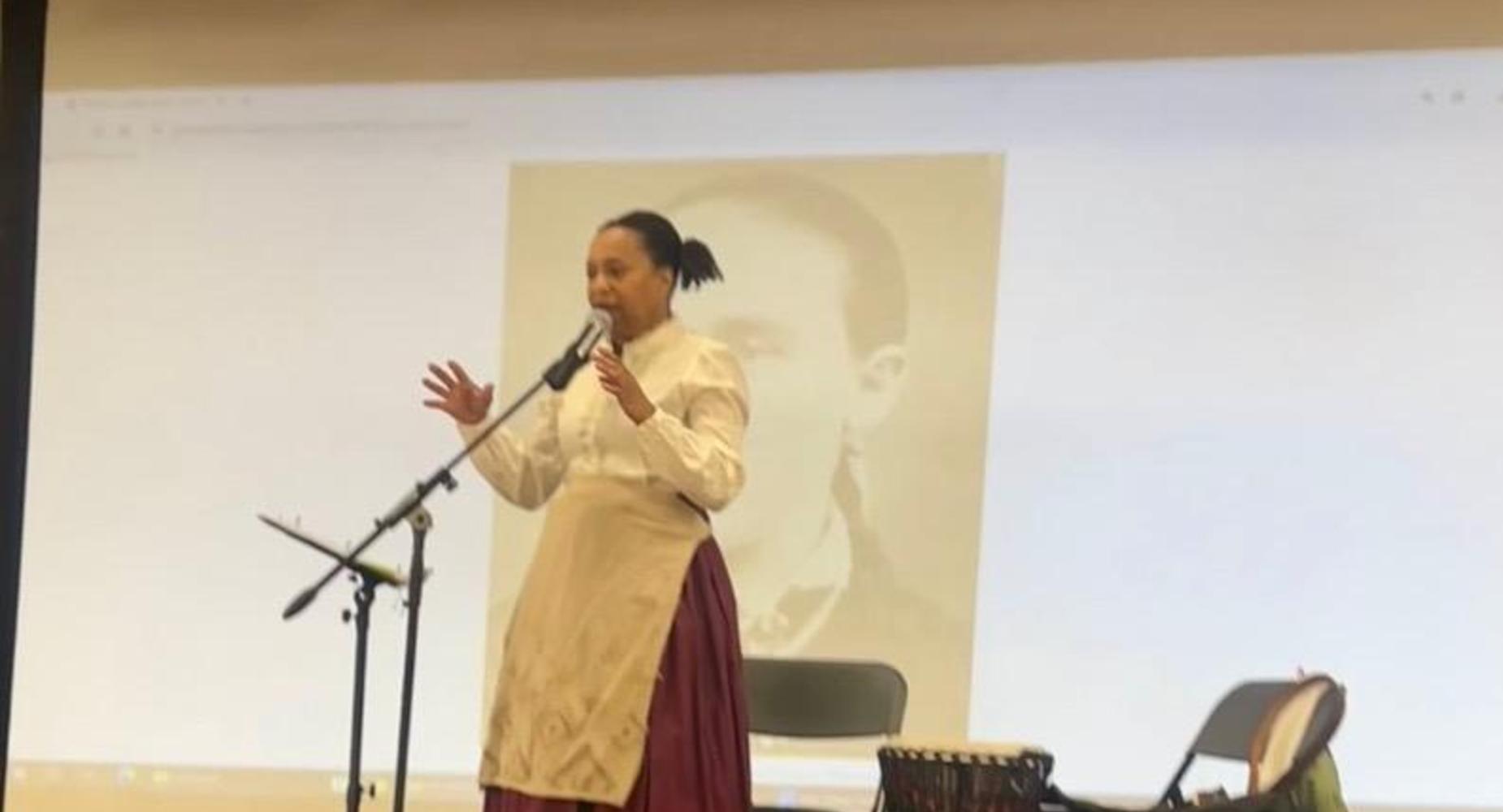 Guest speaker at the microphone on the stage in the auditorium with a photo projected on the screen behind her