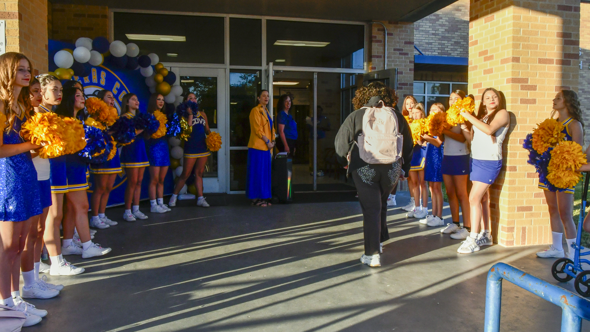 Cheerleaders welcome a student at school, with decorations in the background.