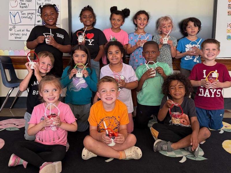 Group of children holding crafts and smiling together in a classroom setting.