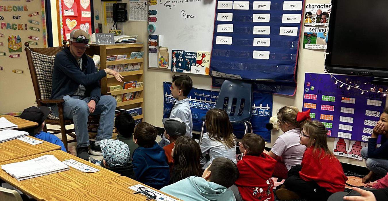 Children sitting on the floor listening to a speaker in a classroom.
