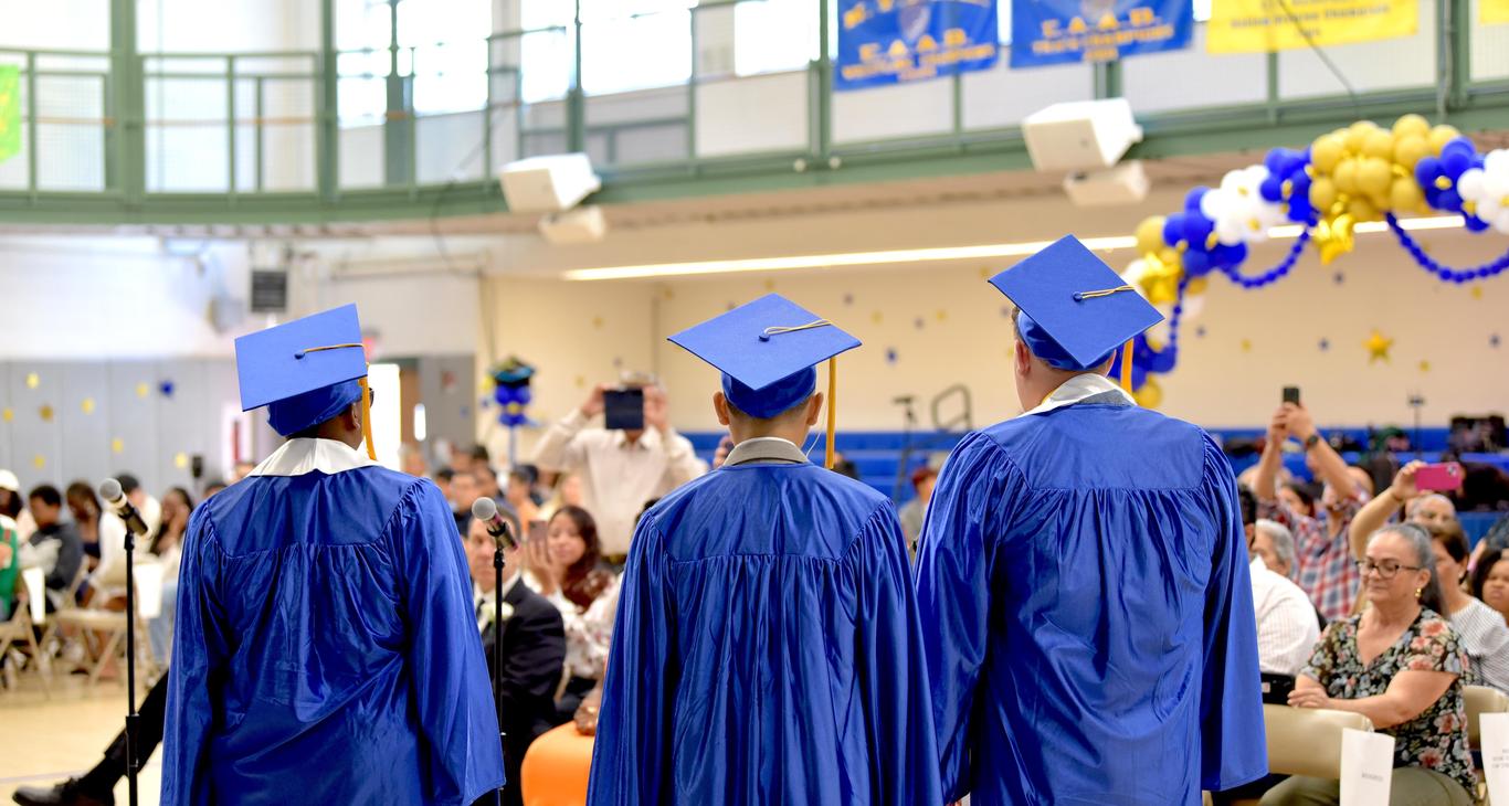Three graduates in blue gowns and caps at a graduation ceremony.