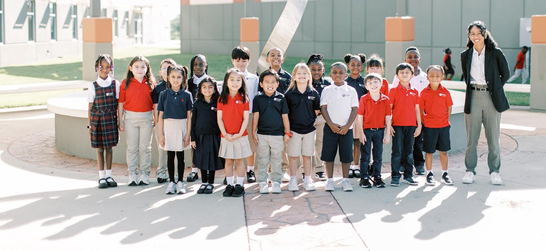 A class of students in uniform standing with their teacher outside the school