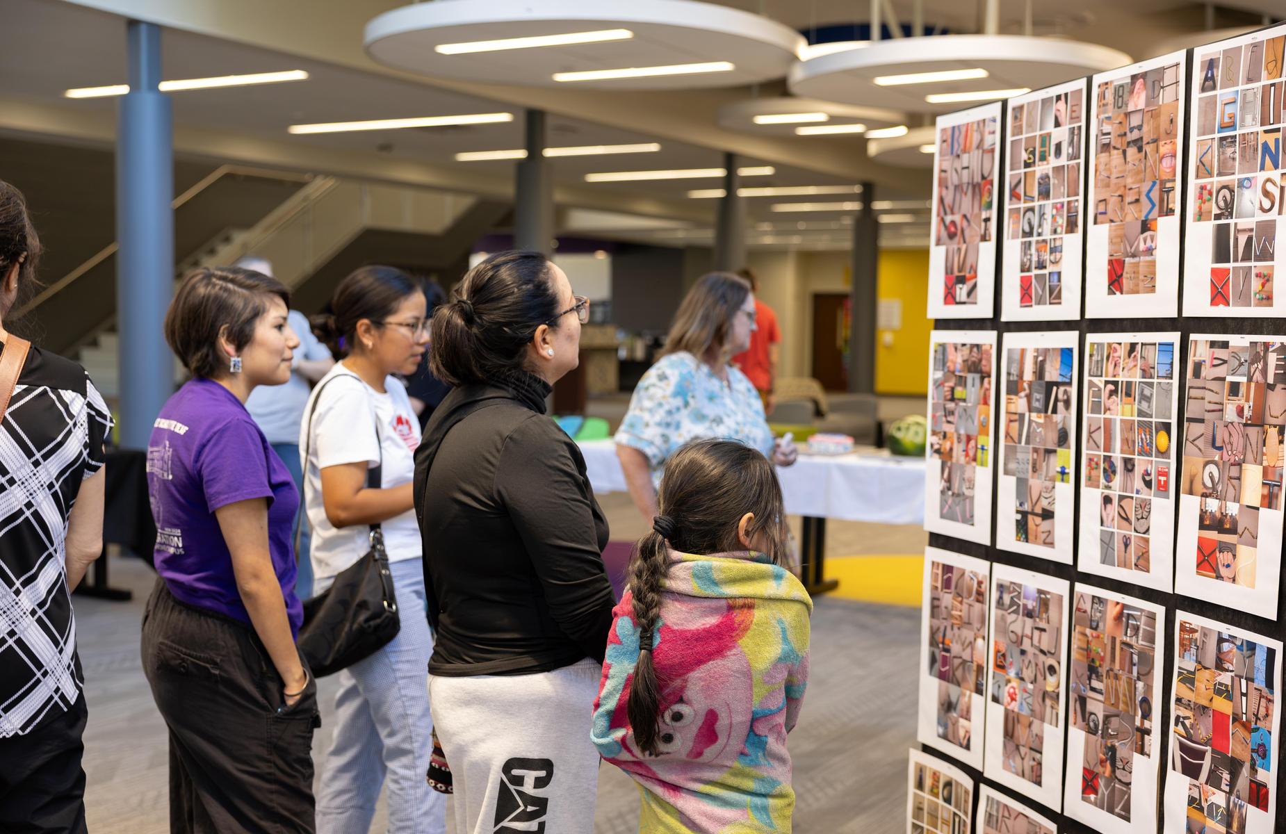 A group of people viewing a collage of photographs in a gallery setting.