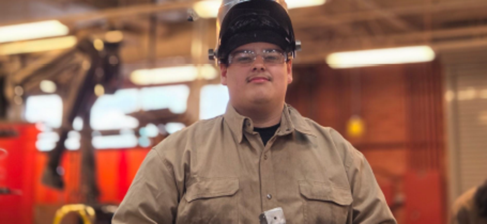 A student wearing safety gear stands under a projector screen displaying a design.