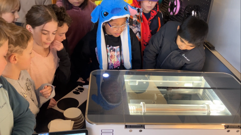 Fourth-grade students surround a Glowforge laser engraver as it engraves pencils with encouraging statements