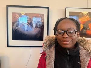 Student in front of their framed artwork on the wall