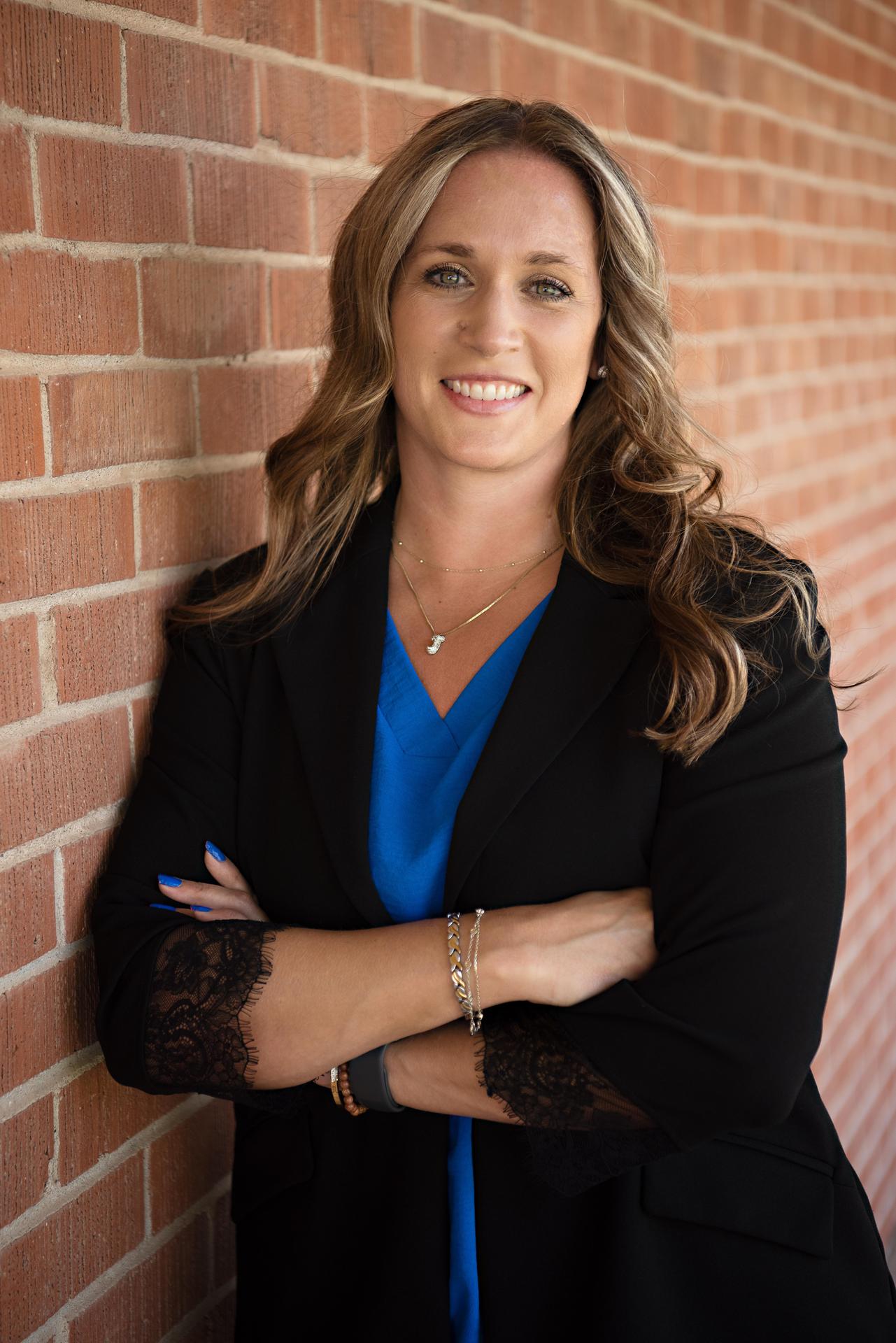Jennifer Bosch in a black jacket with arms crossed against a brick wall