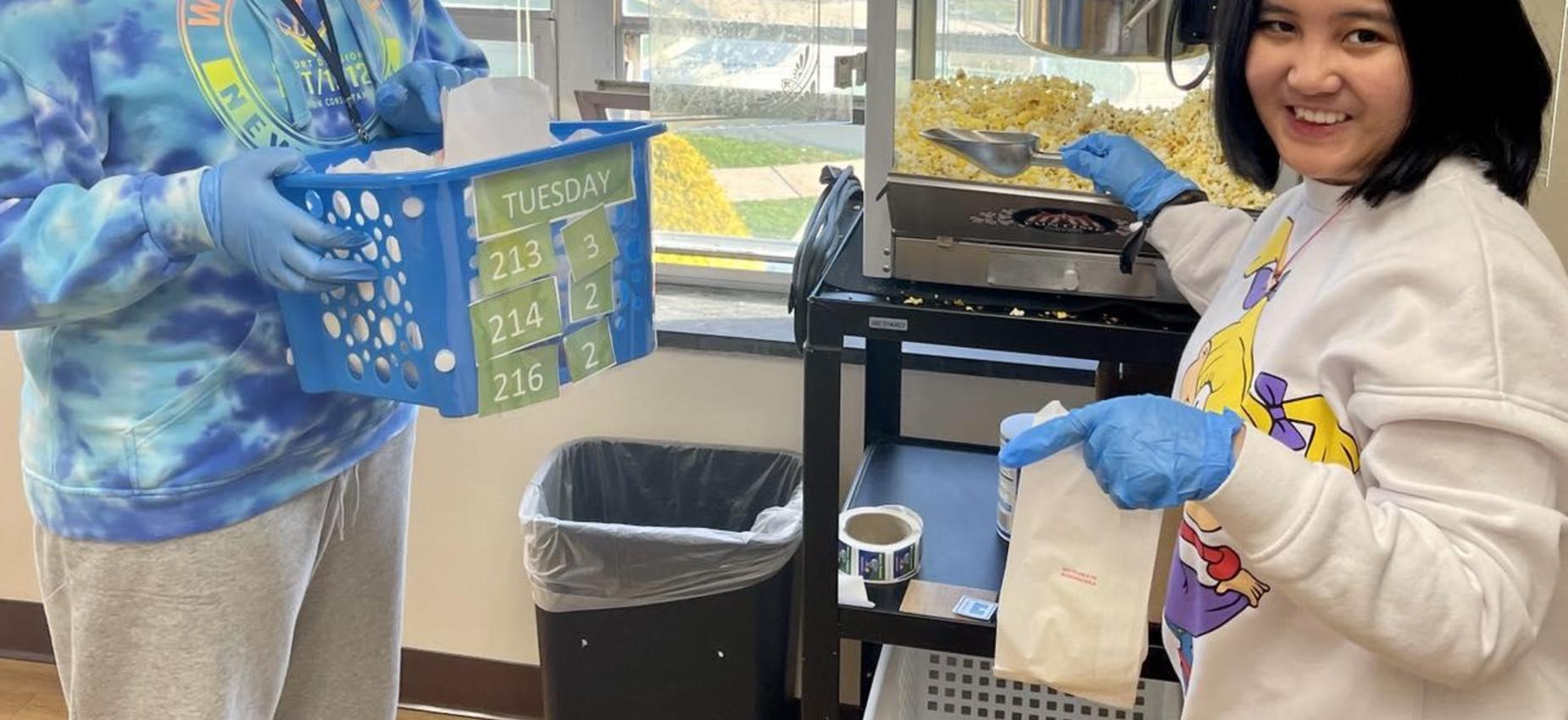 Two individuals preparing popcorn with a basket and smiling indoors.