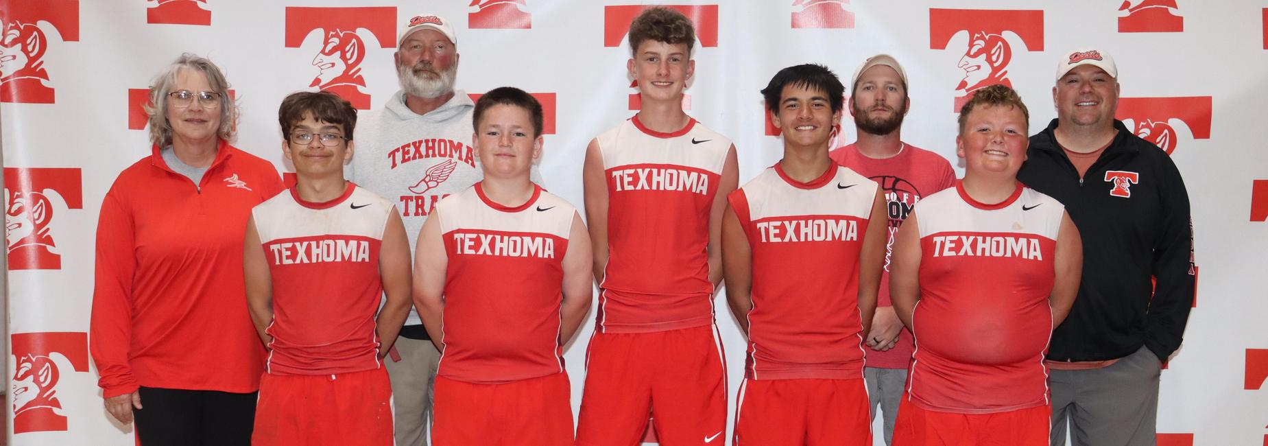 A group of boys in red sports uniforms posing with coaches against a branded backdrop.