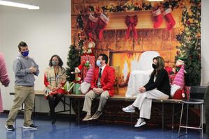 Teacher standing as 3 administrators sit in front of fireplace backdrop