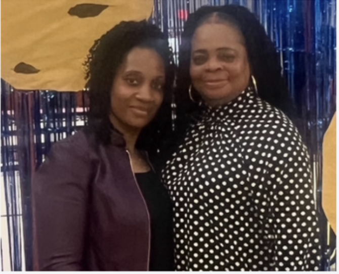 Two females standing close to each other, in front of a yellow background and smiling