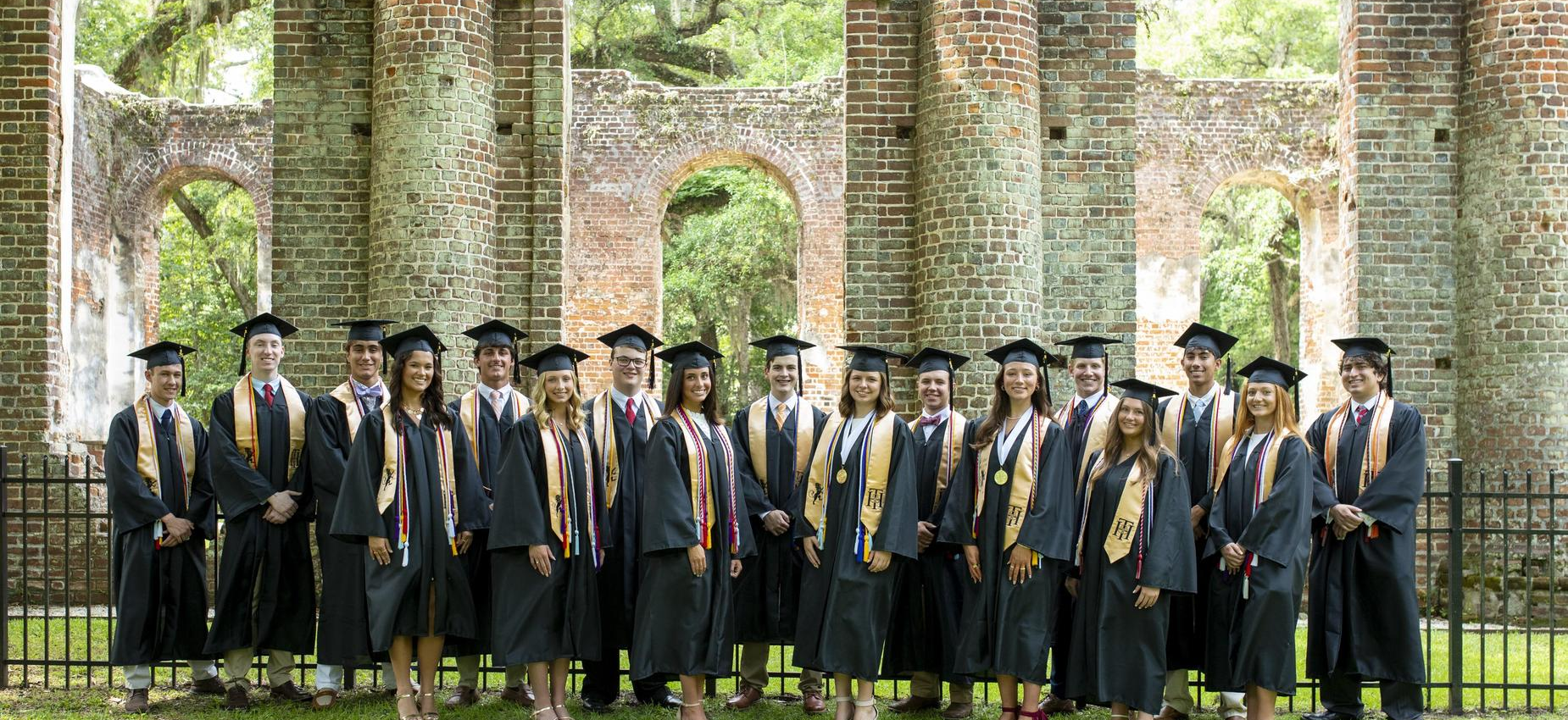 Group of graduates in caps and gowns posing together in front of brick ruins.
