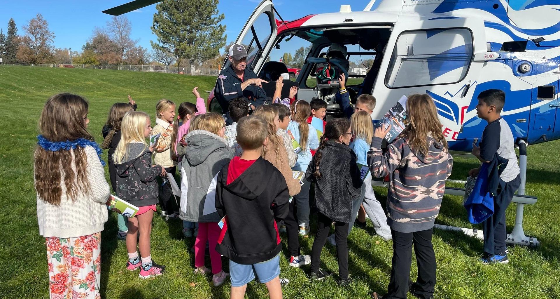 A group of children gather around a helicopter for a demonstration.