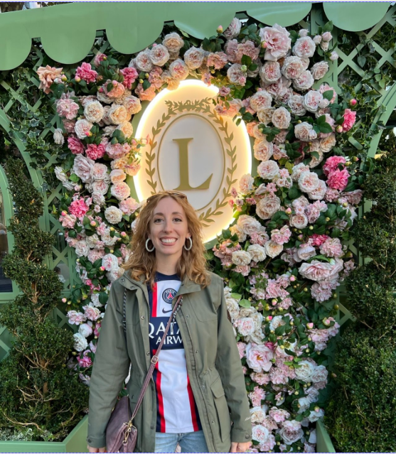  Woman in a Soccer jersey standing in front of flowers with a L in the Middle