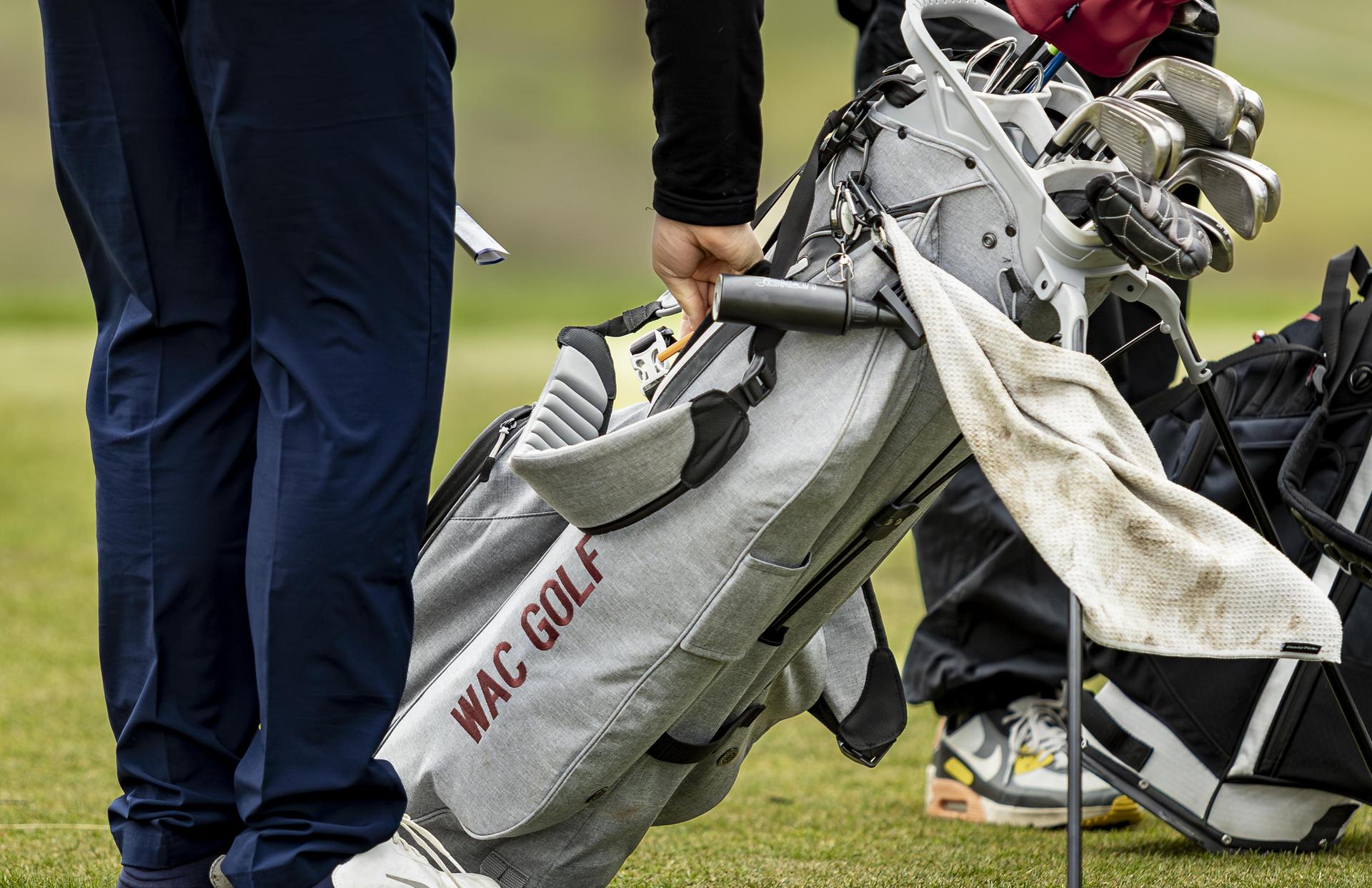 A golfer adjusting a golf bag with clubs on a lush green course.