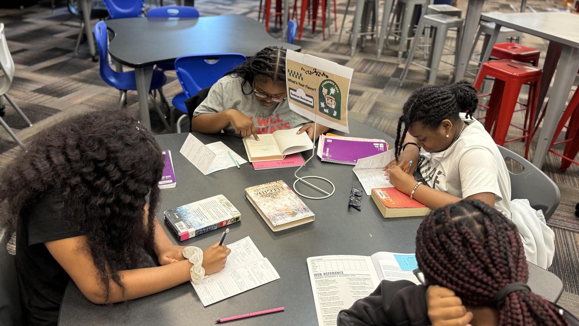 Four students studying at a table with books and notebooks.