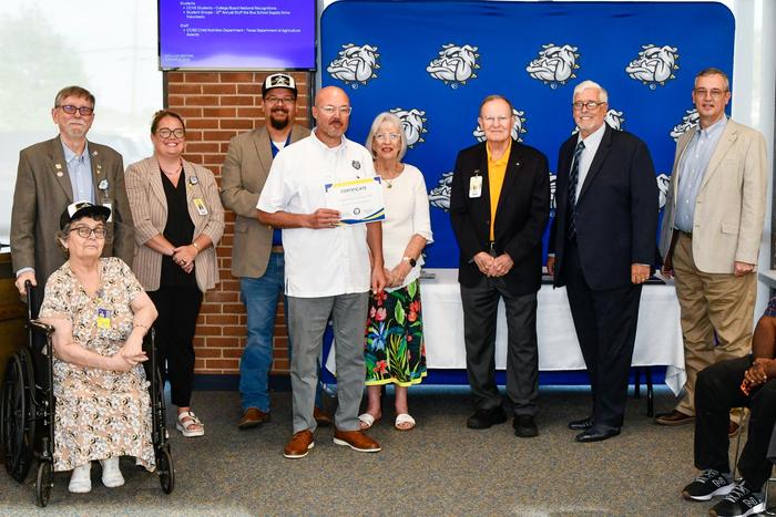 A man and school board members smiling and holding an award