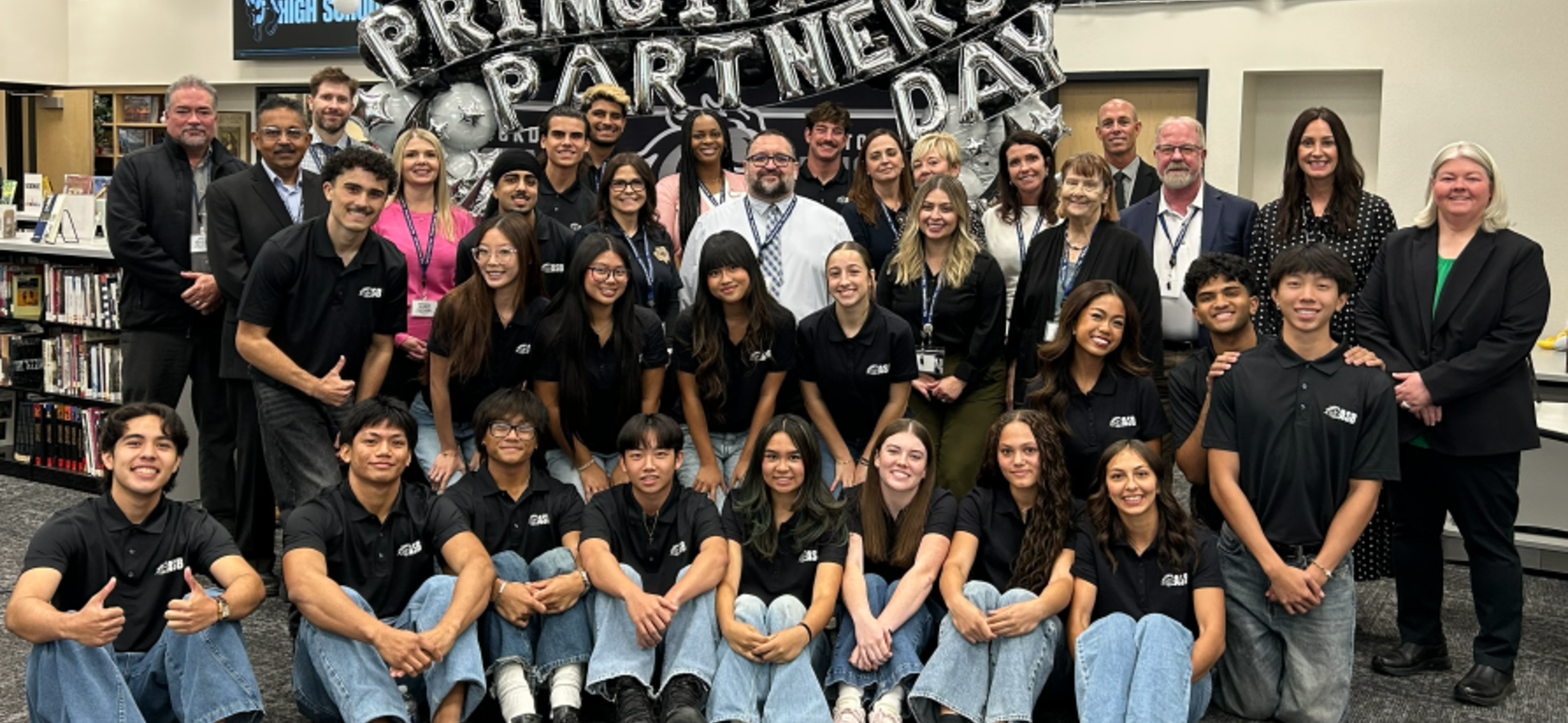 Group photo of students and adults at a partnership event with balloons.