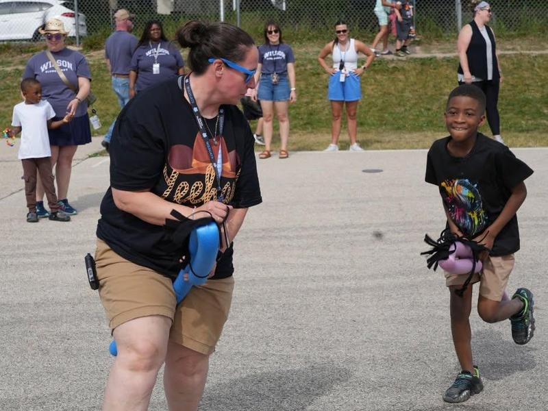 Adult and child running in a playful outdoor activity with spectators in the background.