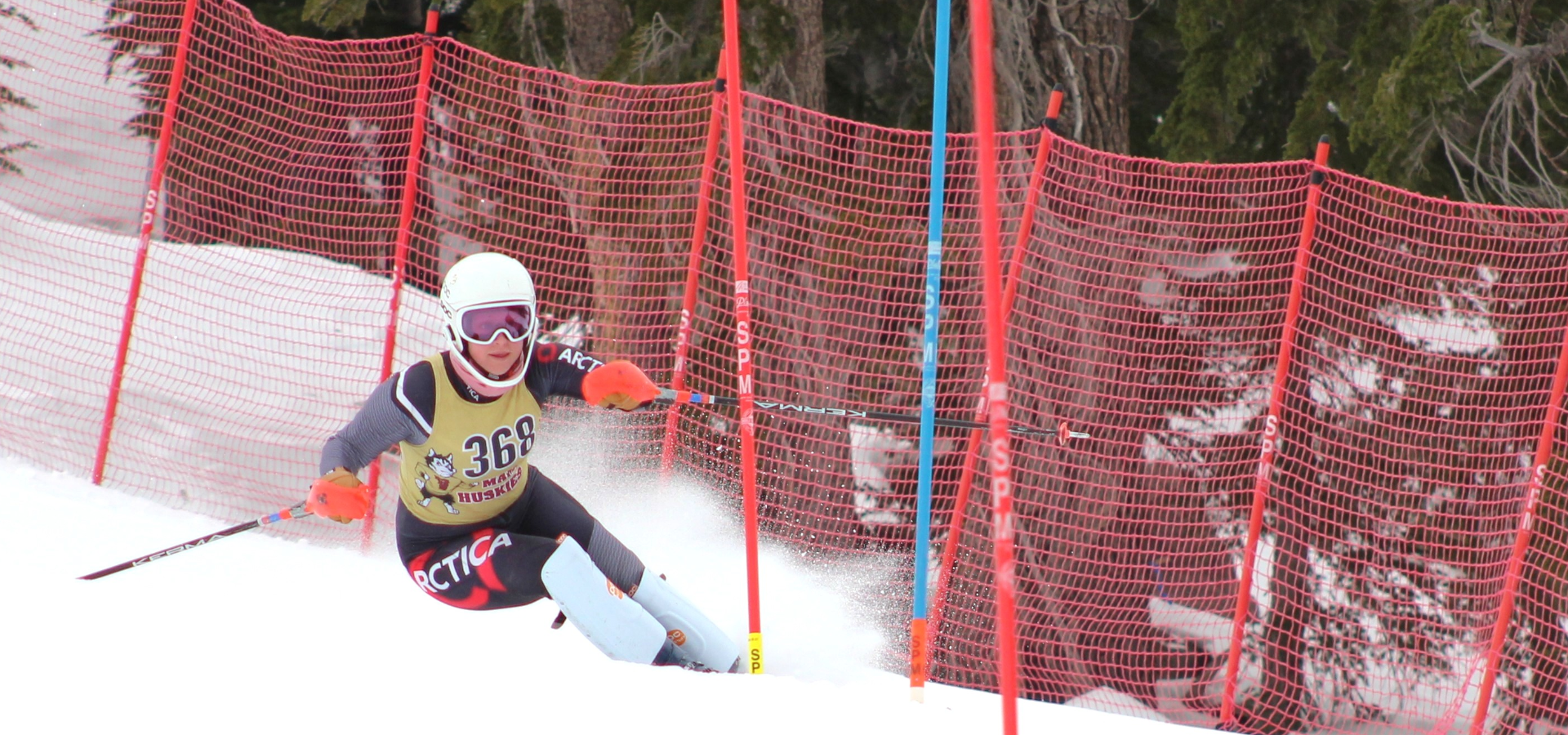 Mammoth High School ski team member on a slalom course with red fencing in the background.