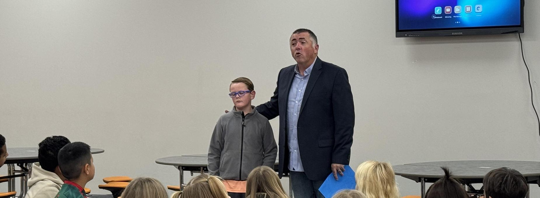 A man speaks to an attentive audience while standing next to a boy.