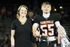 A young man in a football uniform walks with a woman on the field.