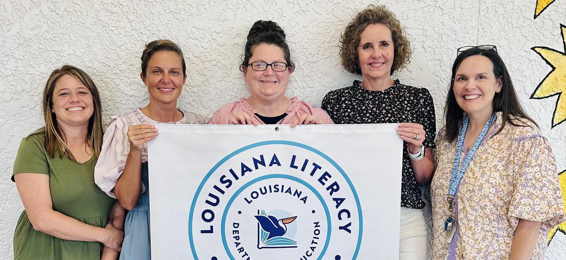 Group of four women posing with a banner for Louisiana literacy leadership recognition.