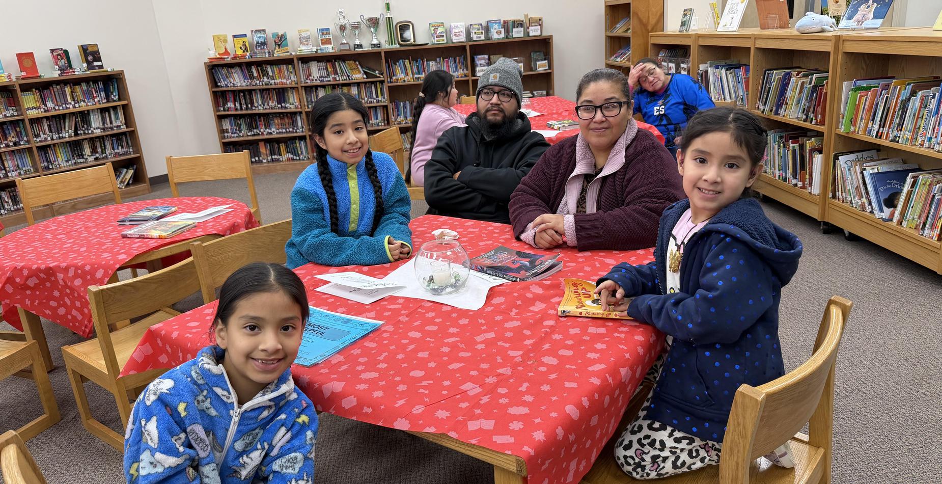 A group of three children and two adults sitting at a table in a library.