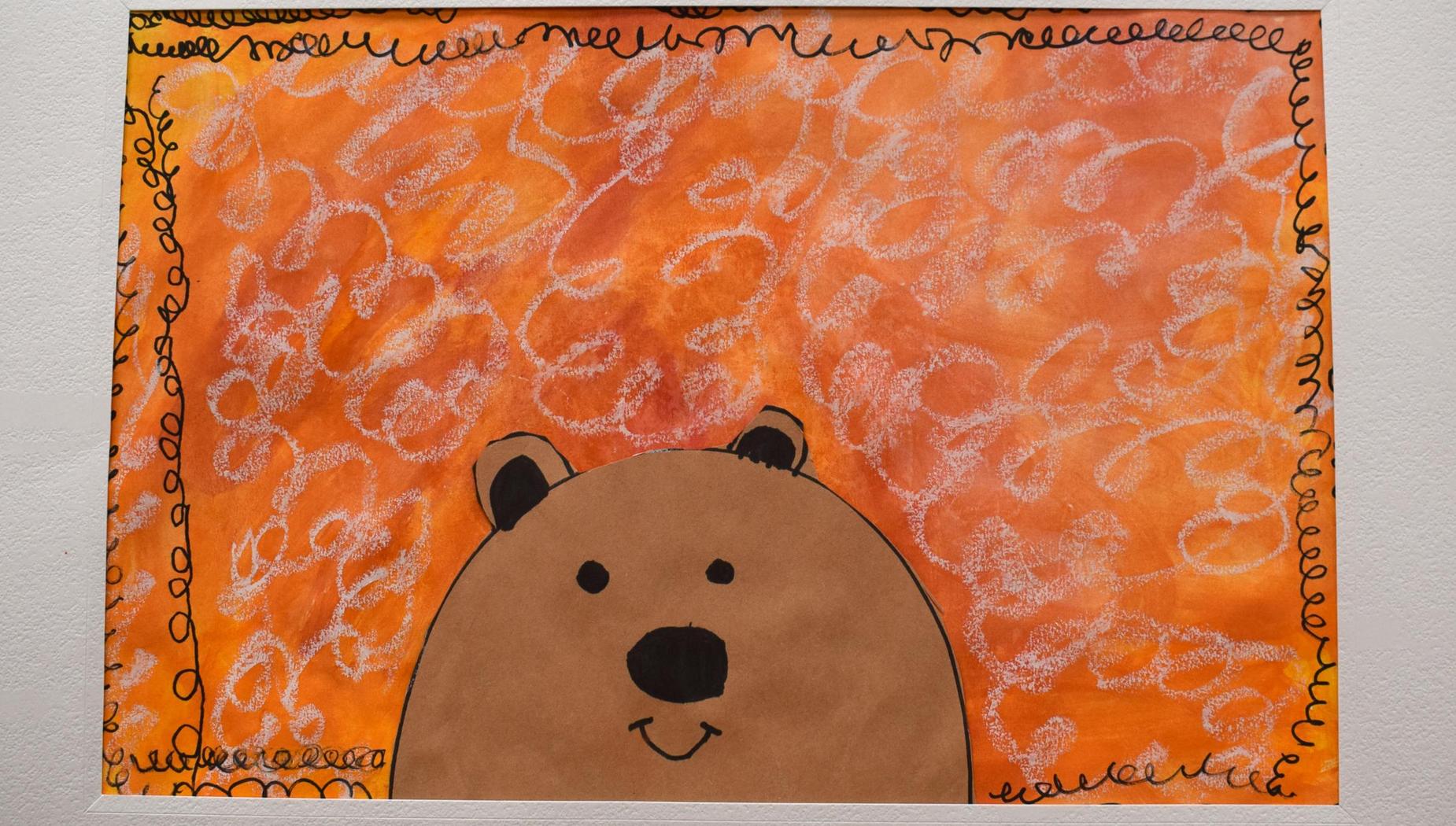 Child's drawing of a bear on an orange background with swirling designs.