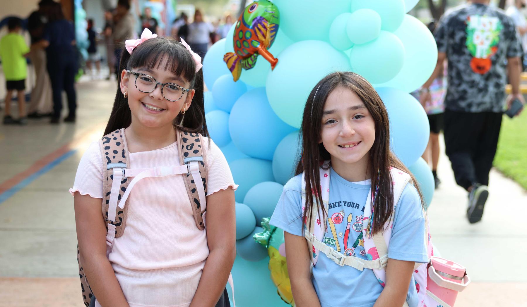 two smiling girls standing in front of a balloon tower.